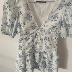 Blommig klänning - Superfin klänning, vit med blå blommor. Toppenskick. Liknande den från Zara. Kom med prisförslag. En lånad bild.   Liten i storlek. Kanske mer xxs.  