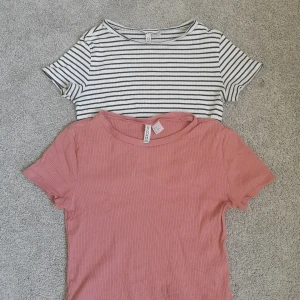 2-pack croppade toppar - 2 stycken snygga croppade toppar. Ena vit och svart-randig och den andra gammelråsa. De är båda i samma modell och är ribbade i storlek M. 