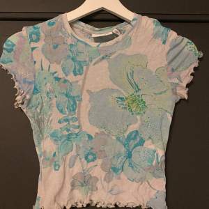 En grön och blå blommig t-shirt i stretchigt mesh tyg. Den har en croppad modell och är från Weekday i storlek XS. Använd ett fåtal gånger och i jättebra skick! 🌷