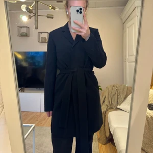Blazerkappa från Filippa K - Fin, tunn kappa i klassisk blazermodell i svart från Filippa K. I fint skick. Storlek 34. Passar för den som har storlek 36 också. Har skärp i midjan som är avtagbart för att få en rakare siluett. Nypris 2999kr 
