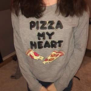 En grå tröja där de står ”pizza my heart” i svart och under det är de två pizza slajsar 