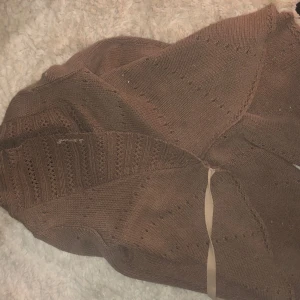 En brun kofta - En brun stickad kofta med snöre och några hål i koftan