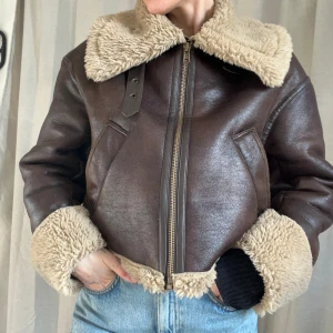 Aviatorjacka i fuskskinn - Jacka från Zara i fuskskinn. Är fodrad med teddytyg så den är väldigt varm och funkar även som vinterjacka. Modellen är boxig och kort. Snygga detaljer med spännen. Knäpps med dragkedja fram. Är i mycket bra skick. 