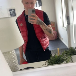 moncler väst - Säljer min röda moncler väst perfekt inför våren, den är storlek 2(s/m)  Den är äkta men har tyvärr inge kvitto då den är 3 år gammal, den är i fint skick och har väldigt bra kvalite.