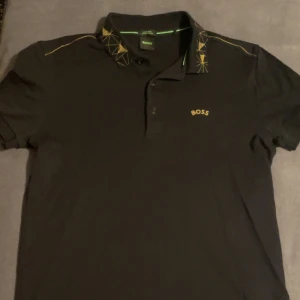 Hugo Boss pikétröja - Hugo Boss pikétröja, storlek S, aldrig använd, svart med gulddetaljer