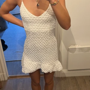 vit miniklänning - vit miniklänning i våfflat material. använd en gång. ganska stretchigt material, stängs med dragkedja i ryggen. den är något längre baktill