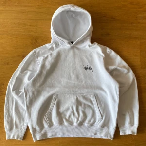 Stussy Hoodie vit - Storlek M från början men har tvättats till ungefär storlek S utifrån egen uppfattning. Skicket är relativt bra men tröjan har ett märke på ena armen (se bild 1) och ett litet hål på ryggen (se bild 4). 