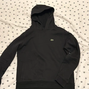 Svart Lacoste hoodie - Hej säljer min snygga Lacoste Hoodie som tyvärr blivit för liten. Den är i perfekt skick och är toppen nu till sommaren. Köpt för orignalpris 899kr