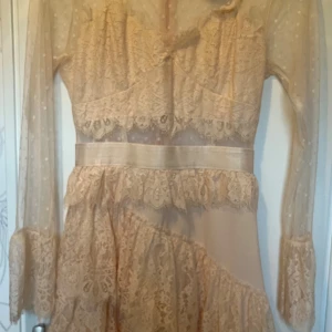 Klänning, spetskläning  - Oanvänd kläning från Danity Paris.  Storlek S Ärmar i tyll med spets. Liv i spets, volanger i spets i kjolen. Hel dragkedja i ryggen.  Färg: peach (aprikos färgad)  Material: 100% polyester  Nypris: 899kr Finns i Askim, Göteborg