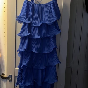 Blå klänning med volanger  - Blå klänning med volanger. Den har tunna band och är öppen i ryggen. Den är enbart testad en gång så aldrig använd. Storlek 38 och jag är 175 cm lång och passar längdmässigt.