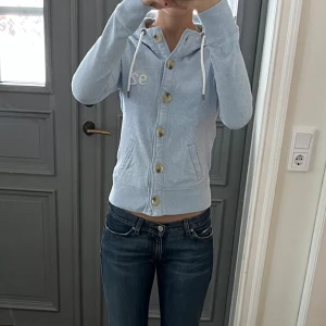 Blå kofta - Blå hoodie med knappar från Abercrombie & Fitch. Storlek S och passar mig som brukar ha S eller M. Fint skick. Använd gärna köp nu!