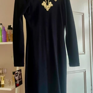 Design klänning Guld/Svart 38/40 - Designad snygg klänning med guldknappar broderier. V formad rygg. Inköpt i Italien. Svart med guld broderier och pärlor. Storlek 38/40