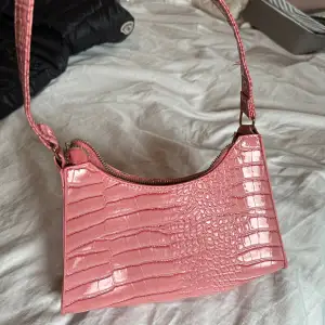 Söt handväska i en fin rosa färg med krokodil inspirerat mönster. Minns inte vart den är köpt tyvärr. Aldrig använd så i perfekt skick. 