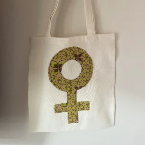 Tygkasse, tygväska, tygpåse  - Handsydd tygkasse med motivet ”feminist”.   Tillverkad i 100% återvunna textilier.   Mått: 32x35 cm  Hämtas på Södermalm alternativt skickas med post. 