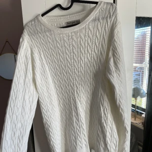 En vit kabelstickad tröja!  - Den är aldrig använd(men prislappen är avklippt). Tröjan har en ganska så slö passform. (Porto tillkommer).