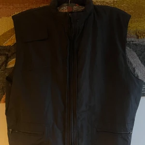 Svart väst - Svart väst med en luva i kragen, man kan väkla ut den och sedan tillbaka med ett fack vid nacken