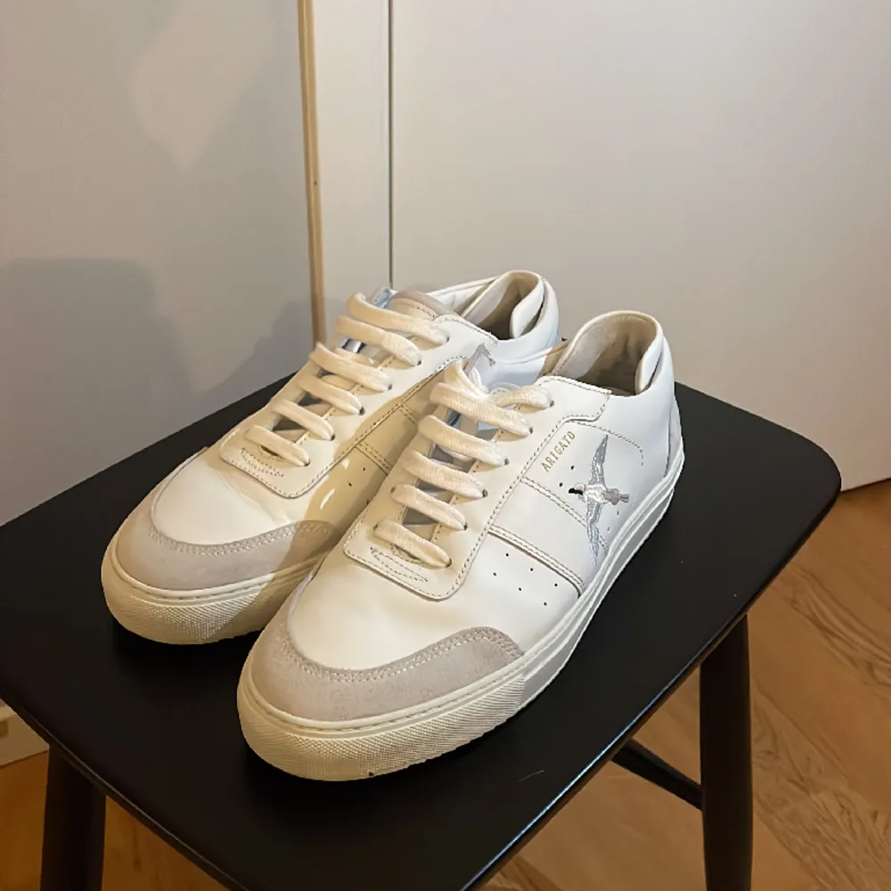 Ett par snygga, vita sneakers från arigato. Nyskick, använda 2 gånger. Storlek 43. Nypris 2650 kr, säljes för 1250 kr.. Skor.