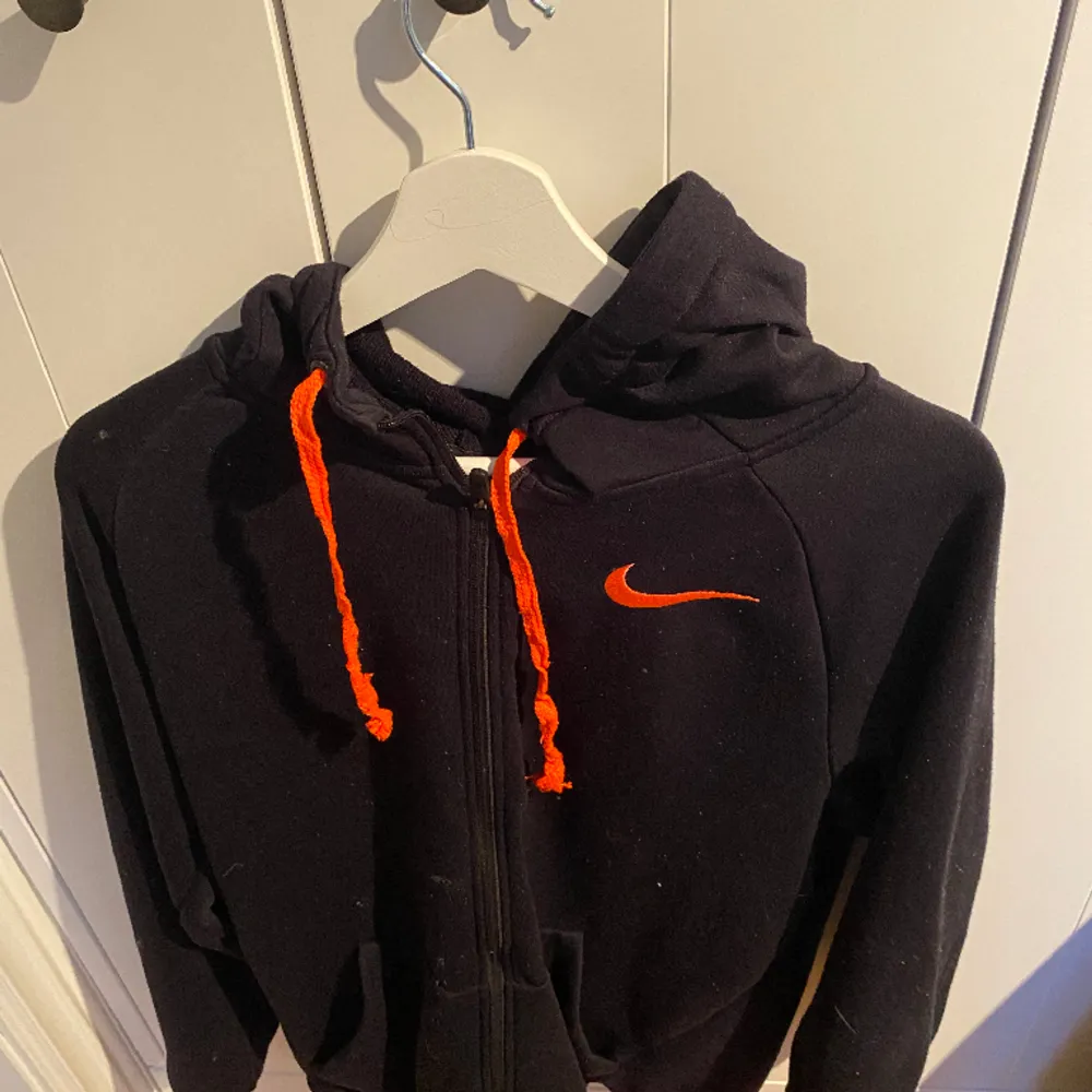 En Nike jacka som är svart med orangea drag och väldigt skön och lite oversized funkar o träna i och styla snyggt . Hoodies.