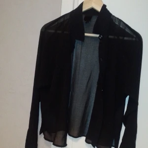 Svart genomskinlig blus med knappar  - Svart genomskinlig blus som man kan ha knäppt eller oknäppt. Mycket bra skick! Monki, strl M men kan även passa S. 
