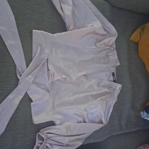 Ljusrosa omlottblus - En elegant ljusrosa omlottblus med långa ärmar och knytband i midjan. Blusen har en v-ringad hals och är tillverkad i ett glansigt material.