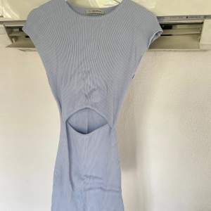 Ljusblå klänning i ett ribbat material, korta ärmar samt en öppningsdetalj framtill vid magen. Använd en gång, i väldigt fint skick.