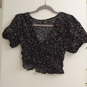 Crop top i mörkt blommönster - Puffiga ärmar och tight i midjan. Crop-top av den något längre typen.
