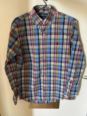 Rutig skjorta från Ralph Lauren - Säljer en klassisk rutig skjorta från Ralph Lauren i blå, grön, röd och vit. Skjortan har lång ärm, knappar framtill och button-down krage. Perfekt för dig som gillar färgglada och tidlösa plagg.