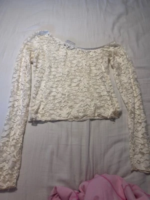 Vit långärmad spetsblus - Säljer en vit långärmad blus i spets med blommigt mönster. Toppen har en croppad passform och är genomskinlig, perfekt att styla med ett linne under. Den har en feminin och romantisk vibe med sina fina spetsdetaljer.
