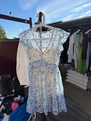 Blommig sommarklänning med volang - Söt vit klänning med blått blommönster och volangdetaljer vid ärmar och nederkant. Klänningen har v-ringning, storlek S från stradivarius🩵🤍 innerklänningen sitter fast