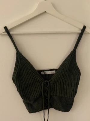 Mörkgrön ribbad stickad linnetopp - Snygg mörkgrön stickad linnetopp från Zara med ribbad struktur och smala axelband. Toppen har snörning framtill och en croppad passform som passar perfekt till höga jeans eller kjol.
