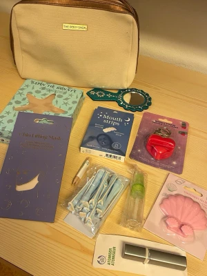 Skönhetskit med necessär och tillbehör - Ett komplett skönhetskit med beige och kopparfärgad necessär från The Body Shop, blå glittrig spegel, rosa hjärtformad mobilhållare och nyckelkedja, sminkborstar, lockgrejer, påfyllningsflaskor, rosa snäckformad tandborsthållare, chin lifting mask, bath air bonnet, mouth strips och nagelbandstickor. Perfekt för dig som gillar skönhetsrutiner.