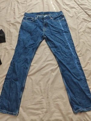 Weekday jeans - Säljer ett par blå jeans med rak passform och fem fickor. Jeansen har normal midja och klassisk denimlook med kontrastsömmar. Perfekta för dig som gillar tidlös stil och enkelhet. Materialet är kraftig bomullsdenim.