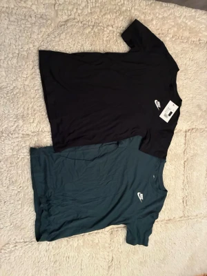 Två stycken Nike t-shirts varav en svart och en mörkgrön - Två stilrena Nike t-shirts i svart och mörkgrönt med klassisk vit Nike-logga på bröstet. Båda har rund hals och korta ärmar. Perfekta till jeans eller shorts för en clean och sportig look. Tillverkade i mjuk bomull för skön känsla hela dagen + helt oanvända!