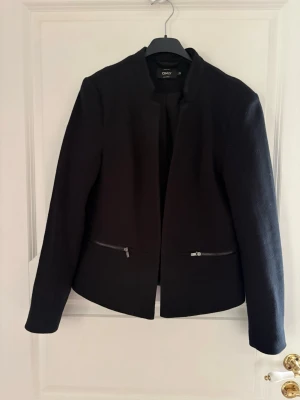 Svart kavaj från ONLY med dragkedjor - Stilren svart kavaj från ONLY med rak passform med modern, asymmetrisk krage och två dragkedjor framtill. Stilren design som passar till många olika looks. Kavajen har en öppen front utan knappar och är tillverkad i ett mjukt tyg som ger en snygg siluett. Perfekt att matcha med jeans eller kjol. Kolla gärna in mina andra annonser❗️