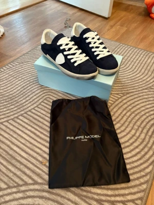 Philippe Model blåa sneakers - Snygga sneakers från Philippe Model i mörkblå mocka med vita detaljer och vita skosnören. Klassisk låg modell med vit sula och logga på sidan. Perfekta för en trendig och avslappnad stil.