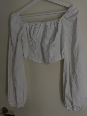 Vit offshoulder croppad blus - Snygg vit offshoulder blus med långa puffärmar och croppad passform. Toppen har resår vid axlar och ärmslut.