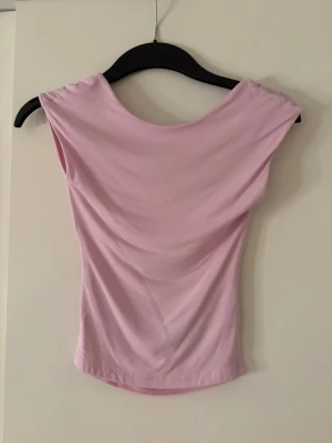 Ljusrosa tshirt  med öppen rygg - Säljer en ljusrosa topp i mjukt material. Toppen  har en snygg öppen rygg med draperad effekt. Perfekt för dig som vill ha en enkel men ändå unik topp till din outfit.