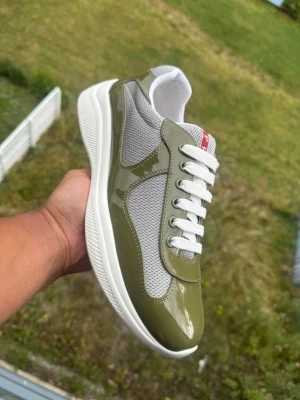 P cups Olivgröna och vita sneakers - Snygga sneakers i olivgrönt och vitt med glansiga paneler och meshdetaljer. Skorna har vita snören och en tjock vit sula som ger en modern look. Perfekta för dig som vill ha något stilrent men ändå unikt i din skogarderob.