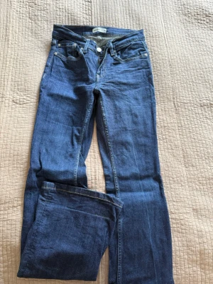 Mörkblå bootcut jeans från Perfect Jeans - Snygga mörkblå bootcut jeans från Perfect Jeans med klassisk femficksmodell och gul kontrastsöm. Jeansen har normal midja och dragkedja med knapp. Perfekta till en avslappnad stil och passar till det mesta. Lite vita ”snö fläckar längst ner vid benet”. Har oxå haft de vikta där nere men det går att stryka dom så blir de helt jämna ner till.