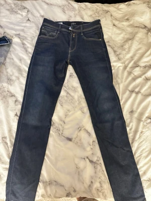 Mörkblå slim fit jeans från Replay - Snygga mörkblå slim fit jeans från Replay, modell Anbass. Klassisk femficksdesign med kontrastsömmar och dragkedjegylf. Jeansen har en modern passform och är tillverkade i stretchigt denimtyg för extra komfort.