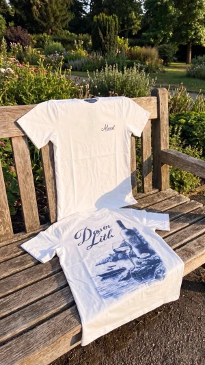 Vita t-shirts med tryck - Två vita t-shirts i bomull. Ena har ett litet broderat tryck med texten 'Marcel' på bröstet, den andra har ett stort blått motiv med texten 'Dysor Lith' och illustration av flaska och natur. Perfekta för en avslappnad stil.