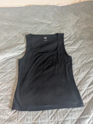 Svart tanktop från lager 157 - En enkel och stilren svart tanktop från 157 med breda axelband och rundad urringning. Tillverkad i mjukt material som sitter skönt mot kroppen. 