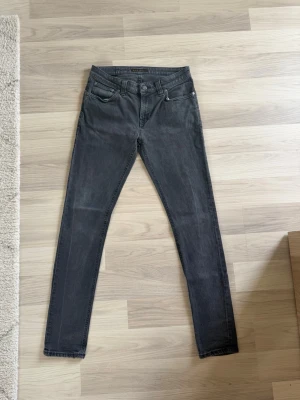 Nudie Jeans - Snygga mörkgrå jeans i slim fit-modell med klassisk femficksdesign och normal midja. Jeansen har raka ben och är tillverkade i ett stretchigt denimtyg som ger skön passform. Perfekta för dig som gillar en stilren och enkel look.