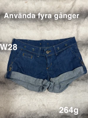 Blå denimshorts från Wrangler W28 - Blå denimshorts från Wrangler med uppvikta benslut och klassisk femficksdesign. Shortsen har snygga knappdetaljer vid fickorna  med broken twill-väv. Perfekta för sommaren och ger en avslappnad look.🌸 Använda fyra gånger. Lappen på insidan är lite trasig. Storlek w28