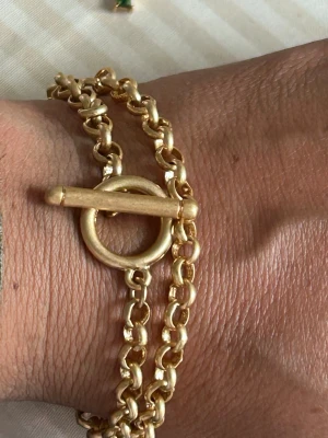 guldarmband med toggle-lås - Snyggt chunky armband i guldfärgad metall med dubbla kedjor och ett stilrent toggle-lås. Länkarna är rundade och ger ett trendigt och robust intryck. Perfekt accessoar för dig som gillar statement-smycken och vill addera lite extra edge till din look.(kan använda som chocker halsband) 