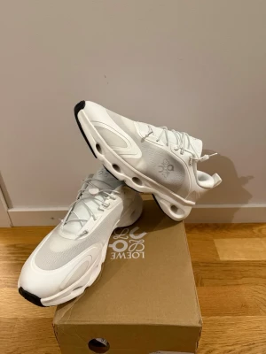 Vita sneakers från Loewe - Snygga vita sneakers från Loewe med futuristisk design och unika hål i sulan. Skorna har meshpaneler, detaljer i läder och snörning med dragsko. Perfekta för dig som gillar stilrena och moderna sneakers med en twist.
