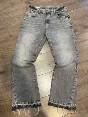 Flared jeans - Säljer ett par gråa raka jeans med hög midja och fransig, rå kant längst ner på benen. Jeansen har klassisk femficksdesign och en tvättad vintage-look som ger en cool vibe. Perfekta för dig som gillar avslappnad stil.