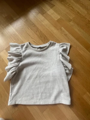 Ljusgrå topp med volangärmar. Funkar för S-L - Supersöt ljusgrå topp med volangdetaljer på axlarna. 