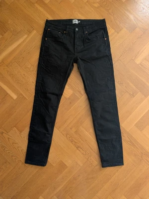 Svarta slim fit jeans - Säljer ett par svarta slim fit jeans med klassisk femficksdesign och knappgylf. Jeansen har raka ben och diskreta nitar vid fickorna. Perfekta för dig som gillar en clean och stilren look.