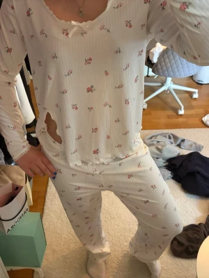 Vit blommig pyjamas med lång ärm - Söt vit pyjamas med små rosa blommor och långärmad tröja. Setet har en avslappnad passform och byxorna är raka med resår i midjan. Materialet är mjukt och ribbat, perfekt för mysiga kvällar. Tröjan har en liten rosett vid halsen och vågig kant. Skriv pm vid funderingar!☺️